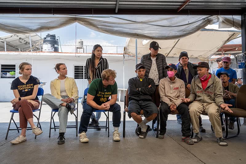 Students and migrants speaking and listening in a circle while seated.