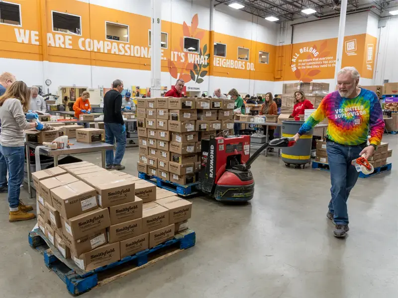 A man in a tie dye shirt pulling a pallet loaded with food at the Northern Illinois Food Bank.