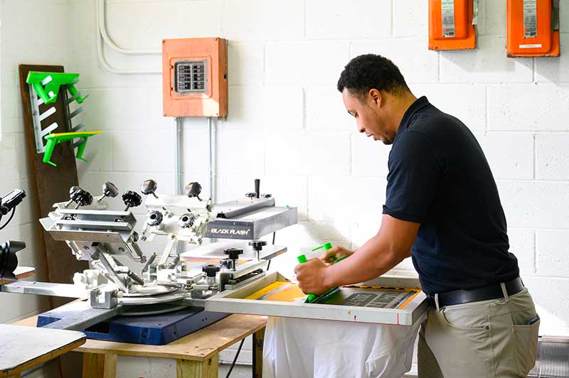 The younger man demonstrates printing on a t-shirt.