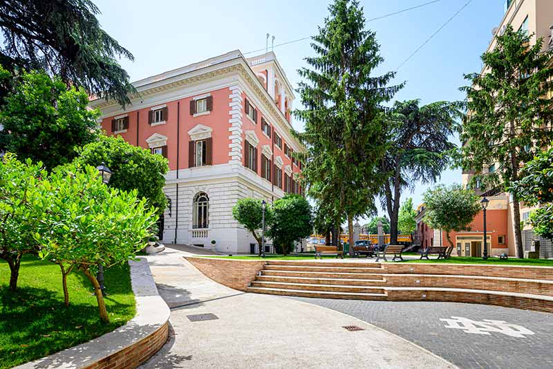 Outside of the Villa surrounded by tall and green trees. On the sidewalk is a painted interlocking ND.