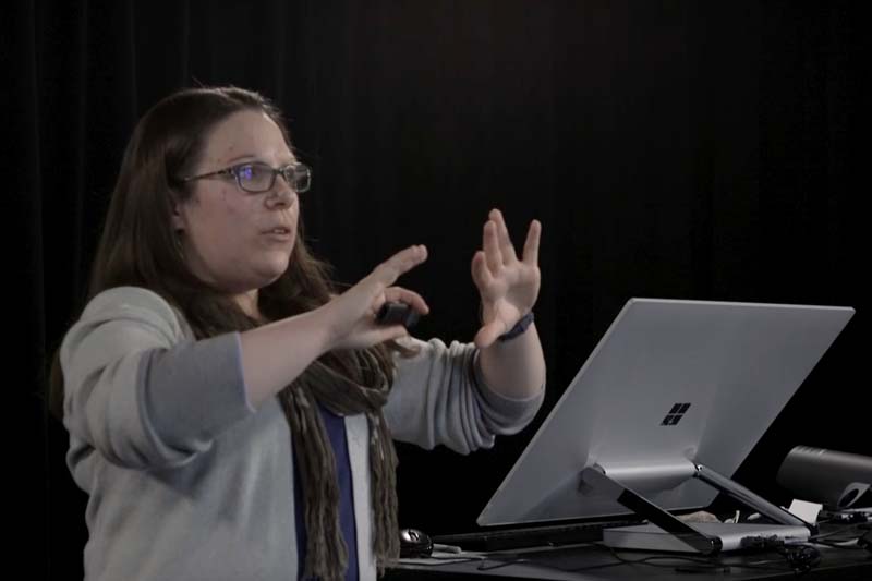 A woman gestures in front of computer.