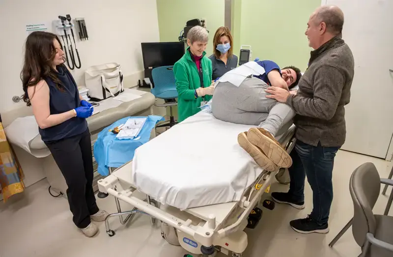 Alec Koujaian lays on his side on a hospital bed. Dr. Elizabeth Berry-Kravis is injecting medicine into his spine.