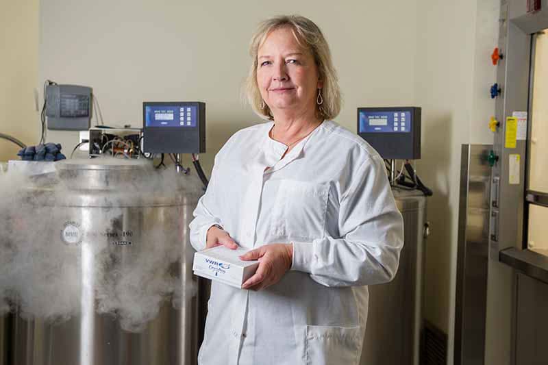 A woman in her white lab coat stands in her research lab