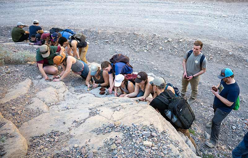 A group of students lean against a rocky slope and take strike and dip measurements.