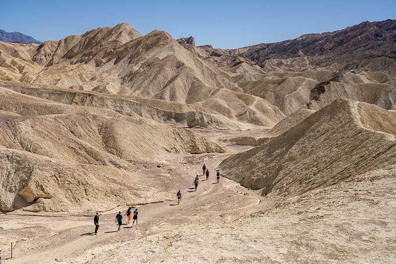 Students hike between bare yellow hills, with blue skies overhead.