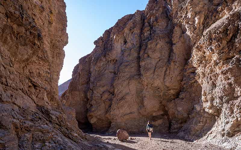 An individual walks between two large rocky moutains.