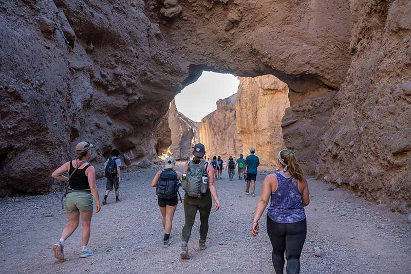 Students walk through vertical canyon walls and under a rock bridge formation.