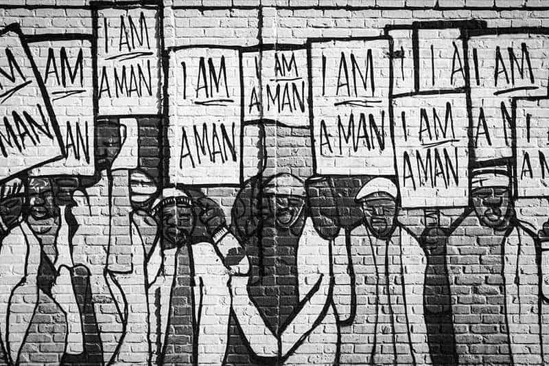 A black and white photo of a painting on a wall. Men hold signs that say 'I am a man'.