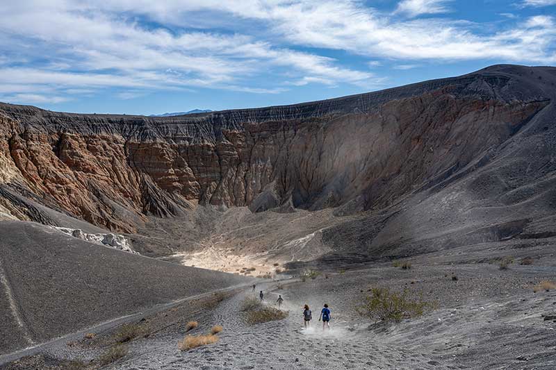 Students run and kick up sand heading down a trail into a large crater.