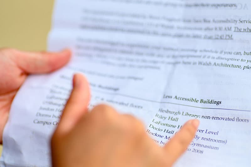 Two hands holding a piece of paper that lists accessible and less acccessible buildings on Notre Dame's campus.