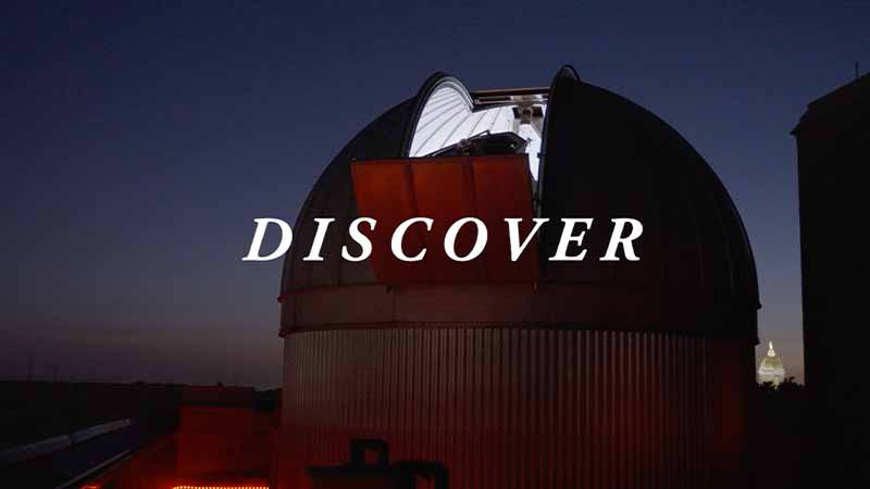A large telescope shines in a dim red light at night. 'Discover' text on top of the image.