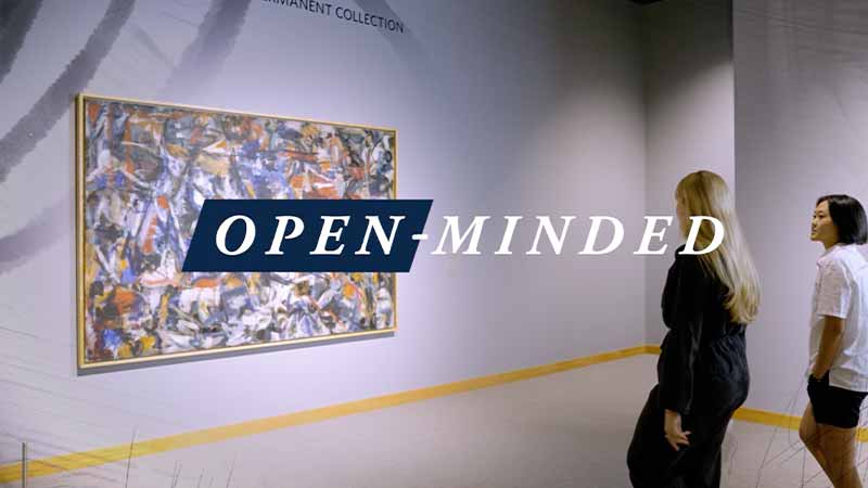 Two people walk towards framed artwork on a wall. 'Open-Minded' text on top of the image.