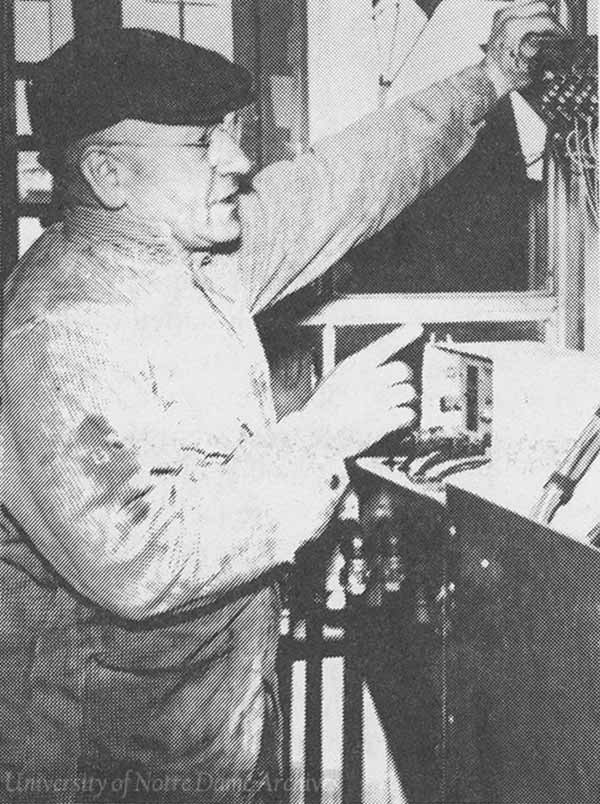 An archival photo of Brother Angelo Trettel, C.S.C. working on electric wiring in a feed center.