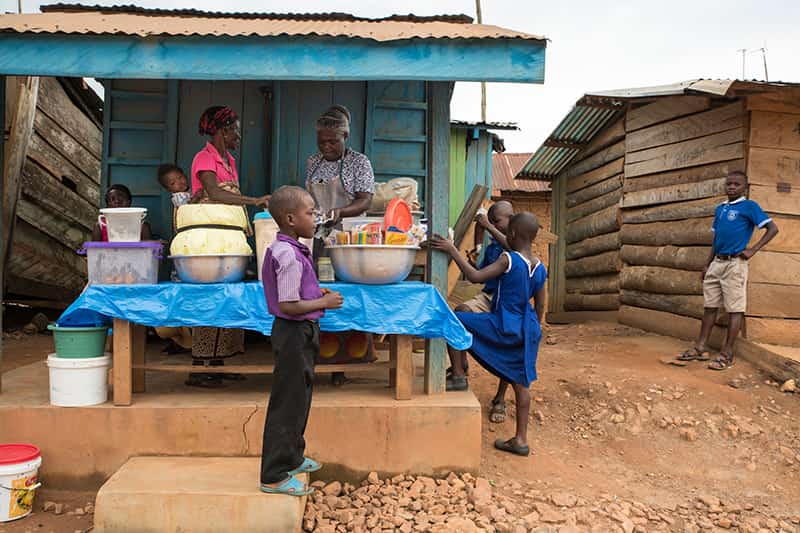 Women prepare lunch for children outside their home.