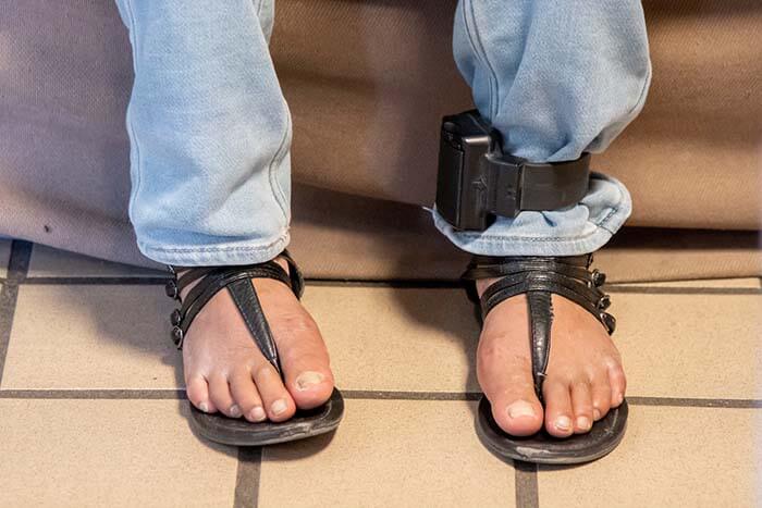 Close-up of feet in sandals, with ankle monitor on the right foot.