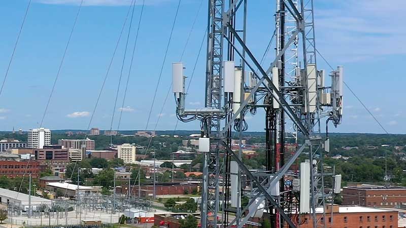 A tall cell tower with several antennas on the outskirts of a city.