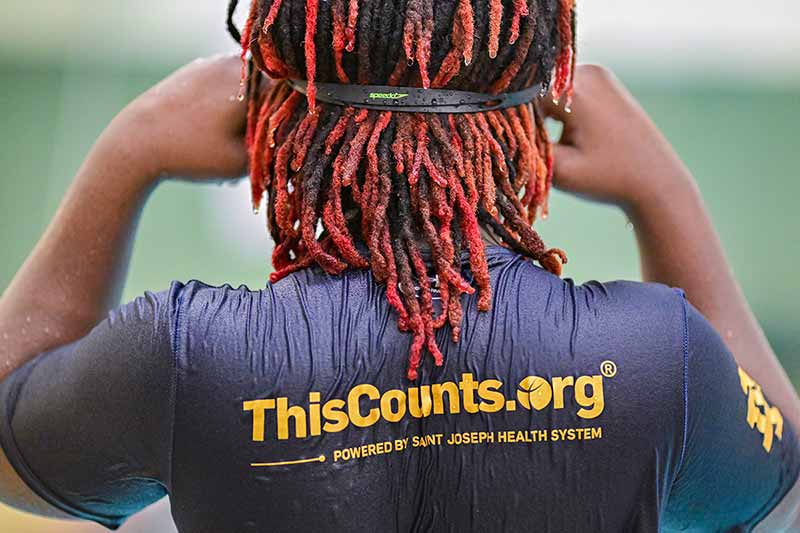 The back of a young boy's head with red-orange dreadlocks adjusts his goggles.