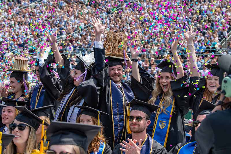Architecture students celebrate and throw colorful confetti in the Notre Dame stadium.