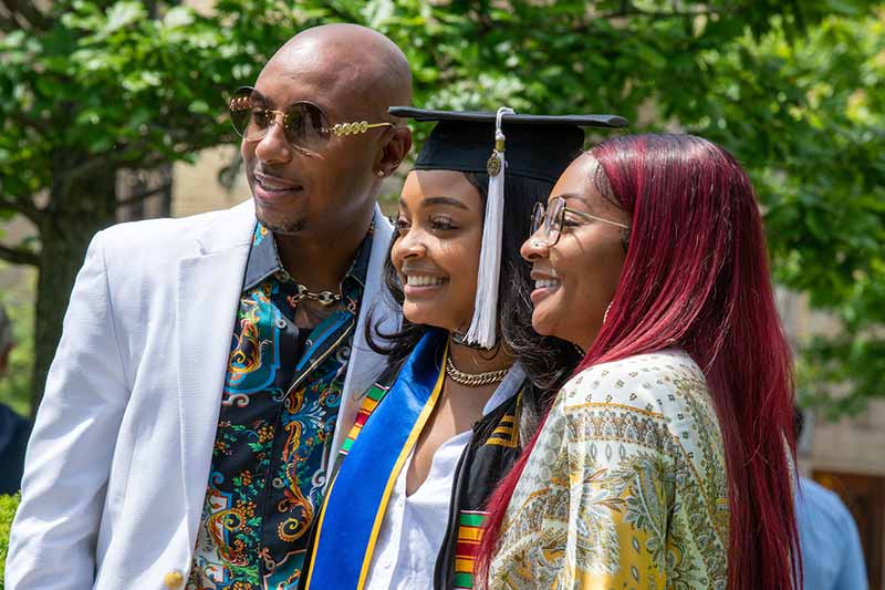 A mother and father take a photo with their recently graduated daughter.