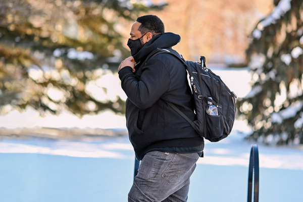 Bettis walks across campus wearing a mask on a snowy day.