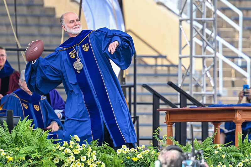 Archbishop Borys Gudziak wearing a navy blue commencement regalia of the University of Notre Dame throws a football during his remarks at the Commencement 2022 ceremony.