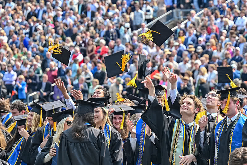 A crowd of graduates throw caps in the air to celebrate graduation.