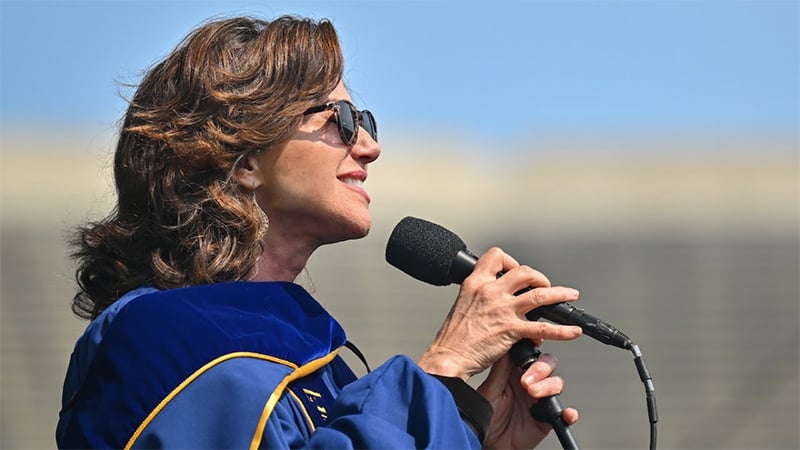 Amy Grant dressed in a doctoral robe singing into a microphone
