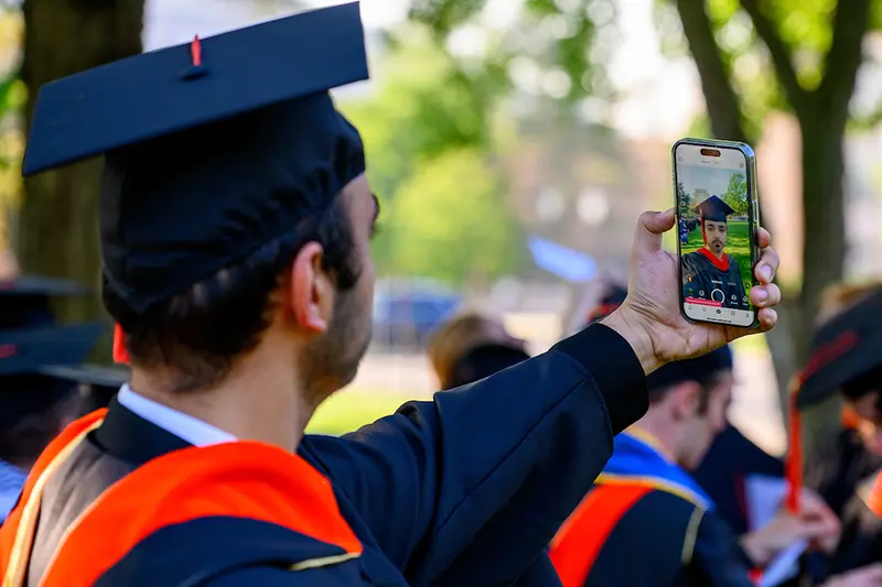 A graduate takes a selfie wearing commencement attire.