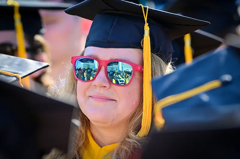 A graduate watches the commencement ceremony wearing reflective sunglasses.