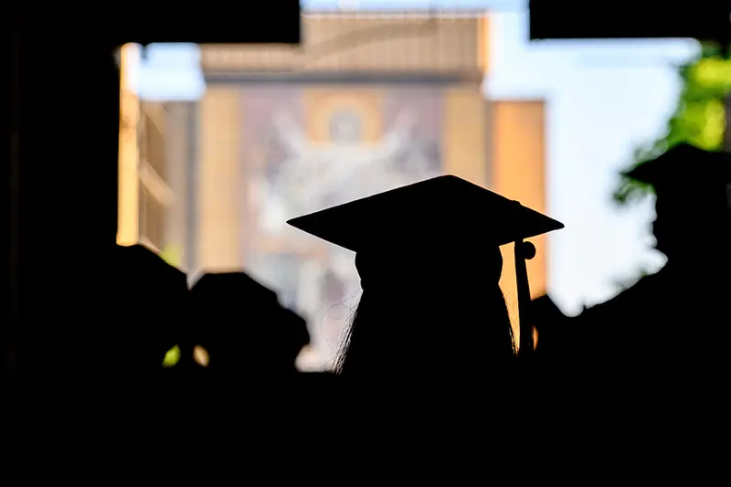 A graduate walks through the stadium tunnel with the library in the background.