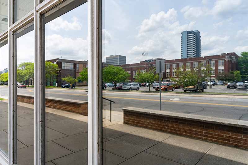 An apartment building and parking lot filled with parked cars reflected on a glass building.