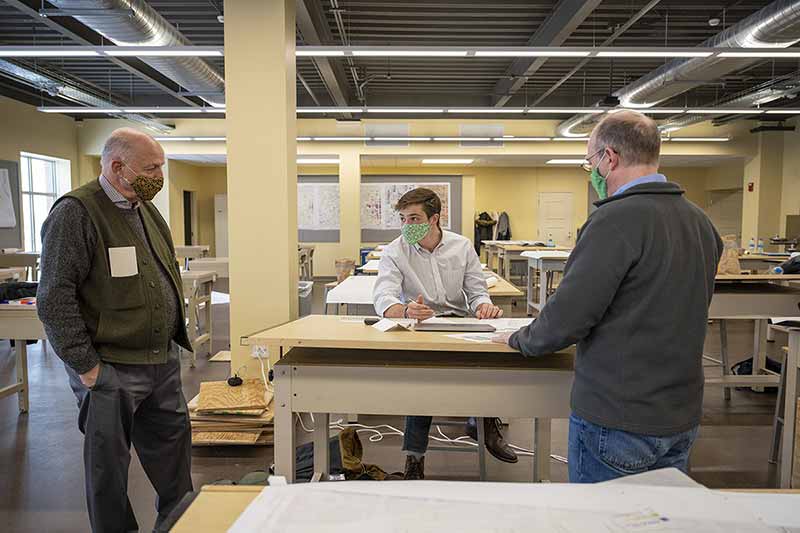 Two professors stand by a student's table while he works.