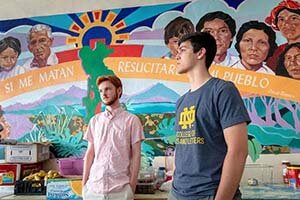 Two students stand in front of a colorful mural.