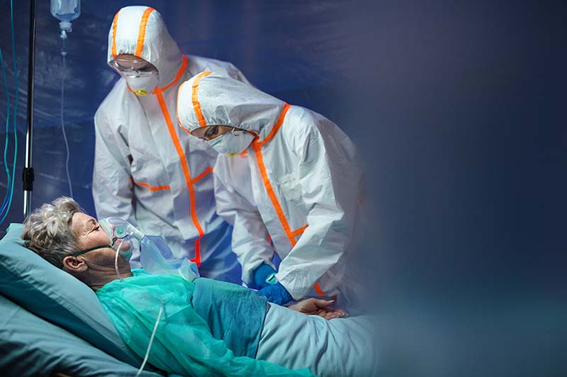 Two doctors in full protective gear look over a female patient.