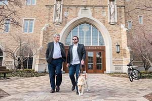 Two men walk, one with a seeing-eye dog.