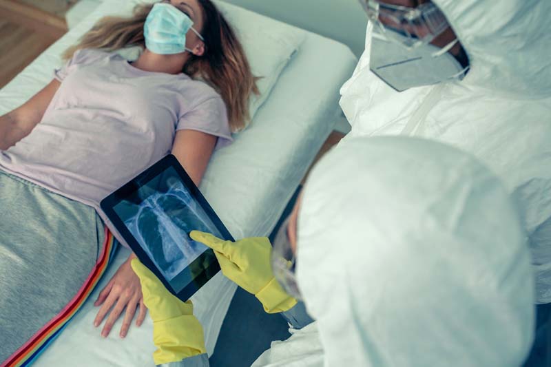 Doctors look at a tablet with lungs on it, over a female patient.