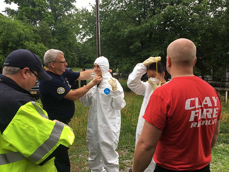 Two students dressed in white full body Hazmat suits, which firefighters around them.