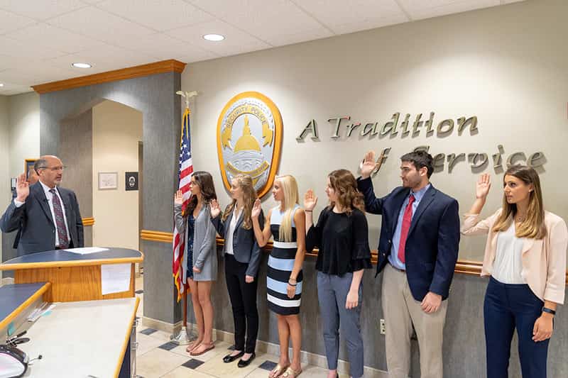 Six students stand against a wall with their right hand raised.