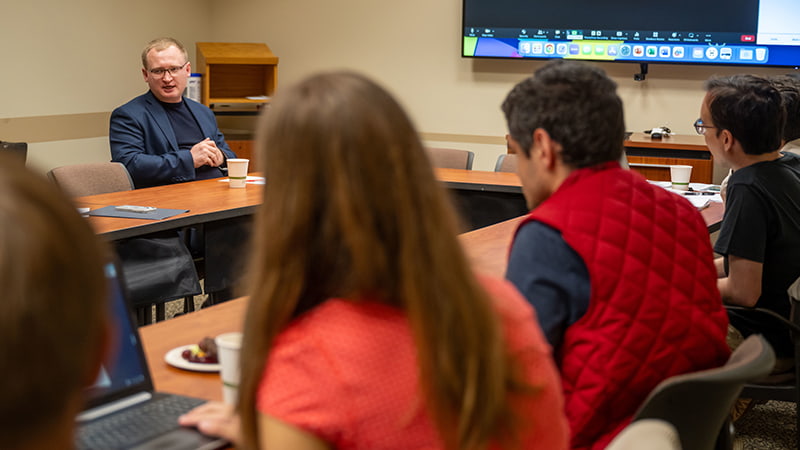 Nazarii Stetsyk sits behind a desk speaking to a row of students.