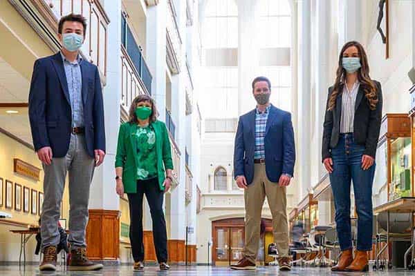 Three students and a professor, all masked, pose in the atrium of Jordan Hall.
