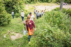 Mothers hold flowers and walk up grassy hill.