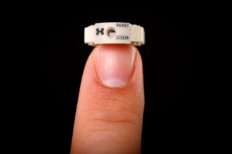 A fingertip balances a small, off-white, ring-shaped device.