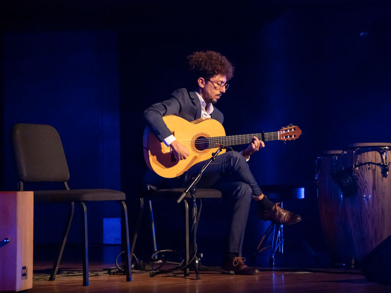 Antonio Herrera plays acoustic guitar onstage.