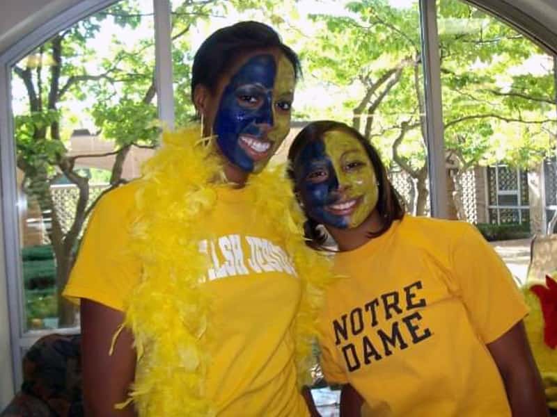 Two girls wearing gold Notre Dame shirts with their face painted half blue and half gold post for a photo.
