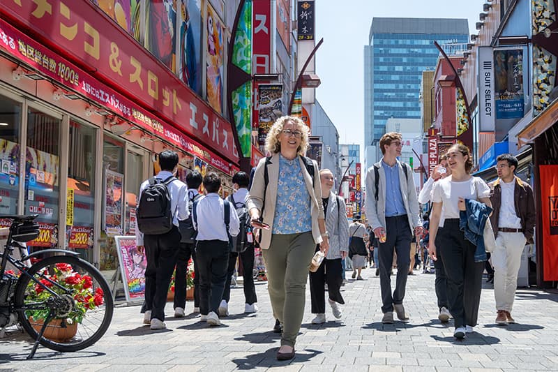 Professor Jessica McManus Warnell leads a group of Notre Dame students along a paved walkway between two rows of shops in Japan.