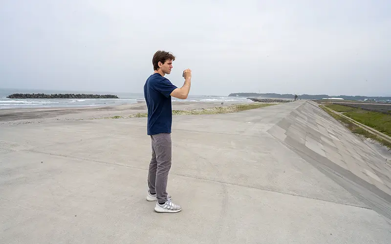 Student standing on the peak of a seawall looking to the right.