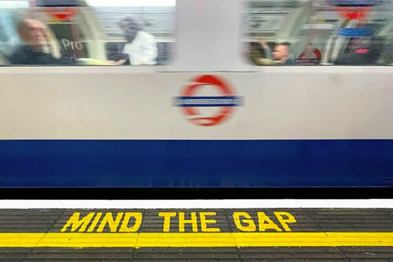 A blurry image of a moving train through the London tube. The words 'mind the gap' are on the sidewalk