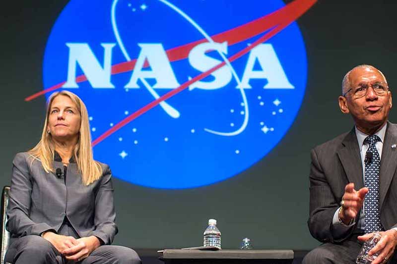 Two people sit on stage. Behind them is a large projected NASA logo.