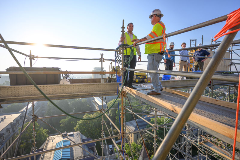 Tony Polotto talk while standing on scaffolding, with a scenic view of campus behind them