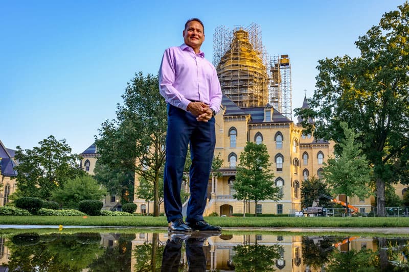 A view of Tony Polotto from the ground. He's standing near a reflective puddle of water and the Golden Dome is in the background.